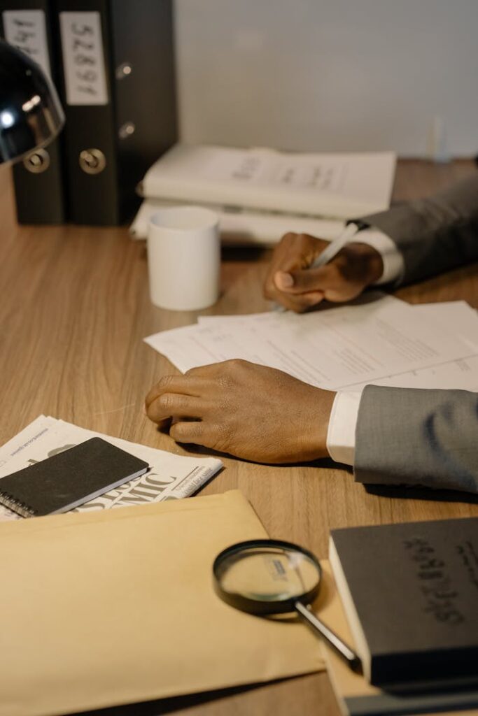 Close-up of a businessman's hands using a pen on documents with a magnifying glass nearby.